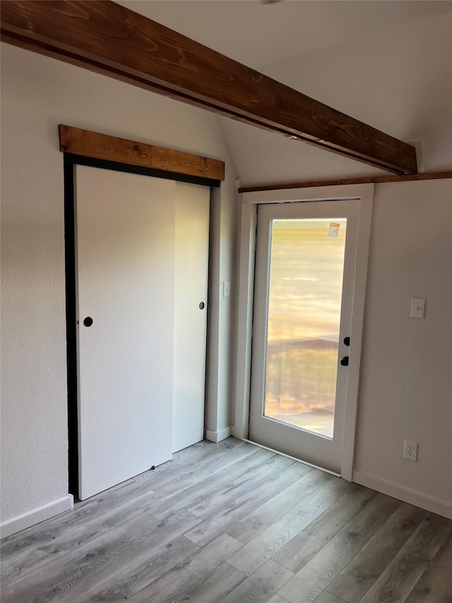 unfurnished room with vaulted ceiling with beams and light wood-type flooring