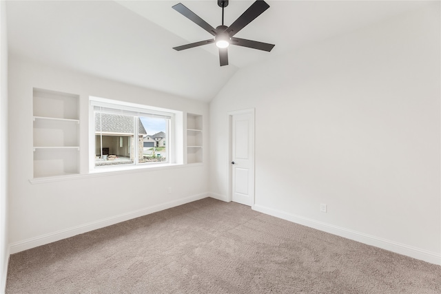 carpeted spare room with built in shelves, vaulted ceiling, and ceiling fan