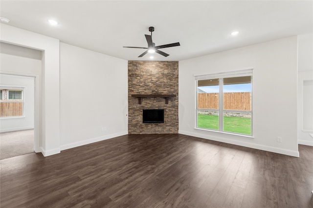 unfurnished living room featuring dark hardwood / wood-style flooring, ceiling fan, and a stone fireplace