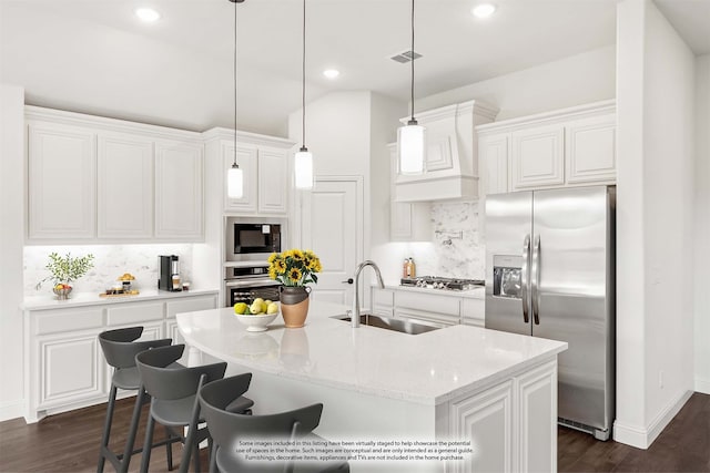 kitchen with appliances with stainless steel finishes, decorative backsplash, white cabinets, light stone countertops, and a kitchen island with sink