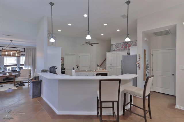 kitchen featuring kitchen peninsula, stainless steel fridge, ceiling fan with notable chandelier, white cabinetry, and hanging light fixtures