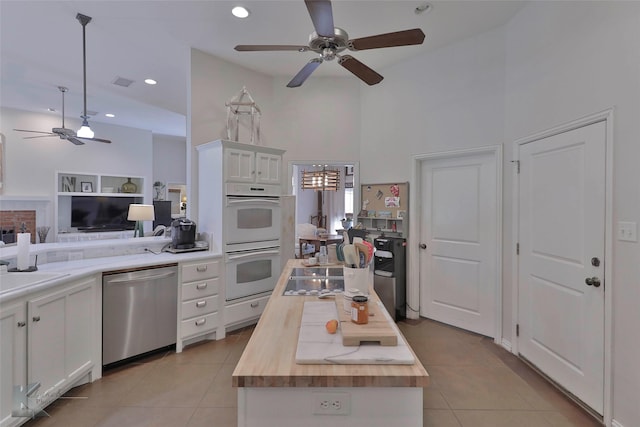 kitchen with stainless steel dishwasher, white double oven, white cabinets, and wooden counters