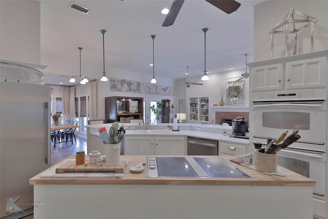 kitchen featuring a brick fireplace, stainless steel appliances, decorative light fixtures, white cabinets, and a center island