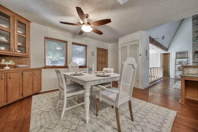 dining room featuring lofted ceiling, a textured ceiling, light wood-type flooring, and ceiling fan