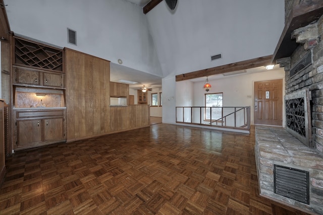 unfurnished living room featuring a large fireplace, dark parquet flooring, beamed ceiling, wooden walls, and high vaulted ceiling