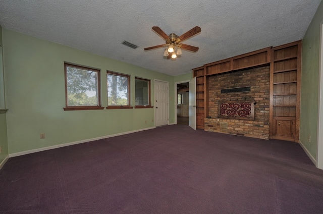 unfurnished living room with a fireplace, a textured ceiling, ceiling fan, dark carpet, and built in shelves