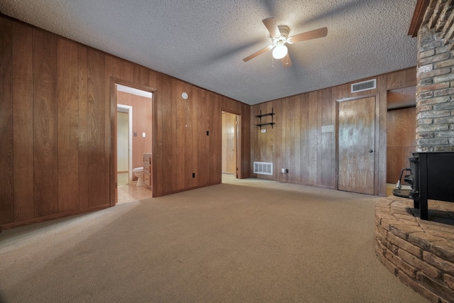 unfurnished living room featuring light carpet, a textured ceiling, wooden walls, and ceiling fan