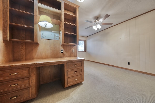 unfurnished office with built in desk, wood walls, light colored carpet, and ceiling fan