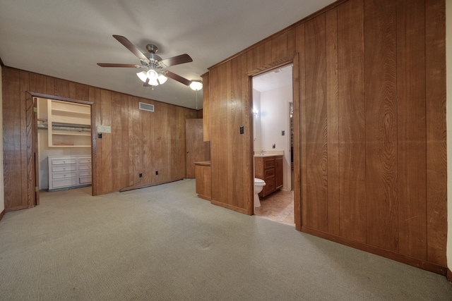 unfurnished bedroom with wood walls, connected bathroom, light carpet, and ceiling fan