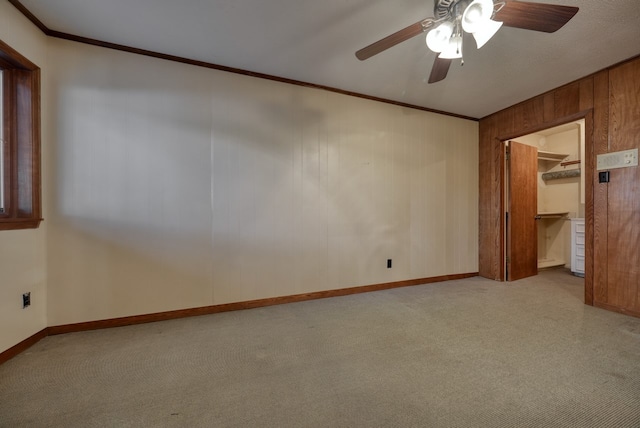 empty room with crown molding, wood walls, and ceiling fan