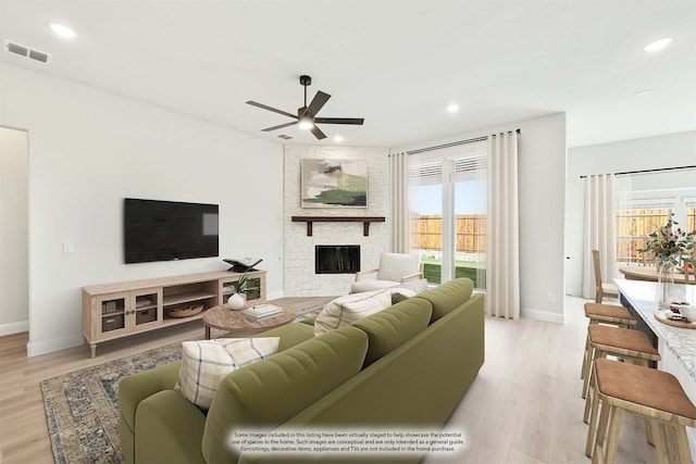 living room featuring ceiling fan, a fireplace, and light hardwood / wood-style flooring