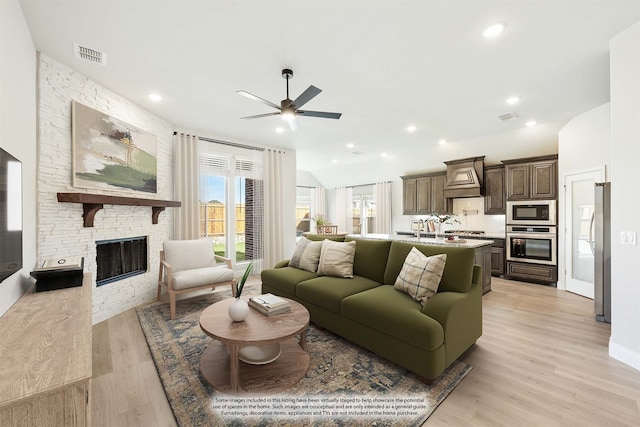 living room featuring ceiling fan, a fireplace, vaulted ceiling, and light wood-type flooring