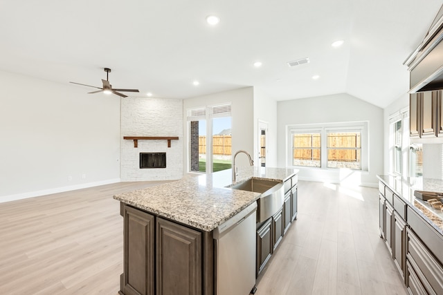 kitchen featuring a stone fireplace, dishwasher, sink, light stone counters, and a center island with sink