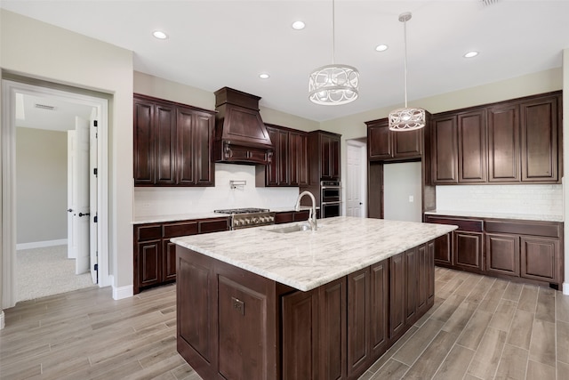 kitchen with a center island with sink, premium range hood, decorative backsplash, light carpet, and sink