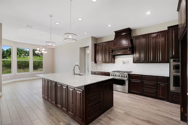 kitchen featuring decorative light fixtures, custom exhaust hood, tasteful backsplash, appliances with stainless steel finishes, and a kitchen island with sink