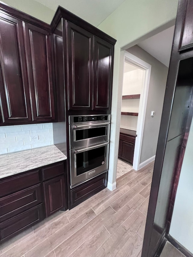 kitchen with backsplash, stainless steel double oven, and light wood-type flooring