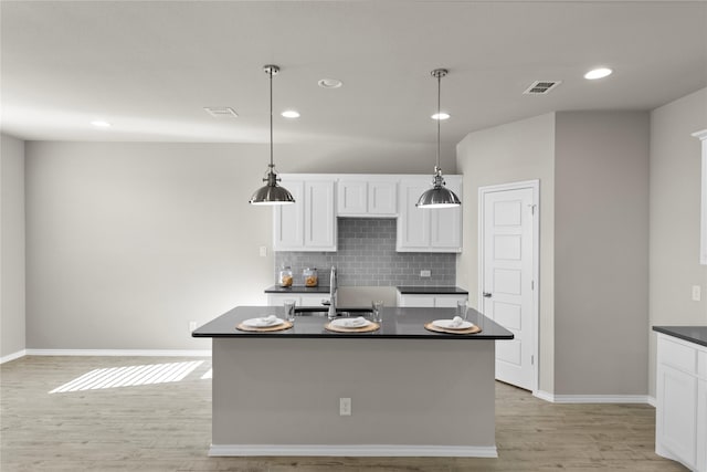 kitchen with pendant lighting, sink, light hardwood / wood-style flooring, a kitchen island with sink, and white cabinets