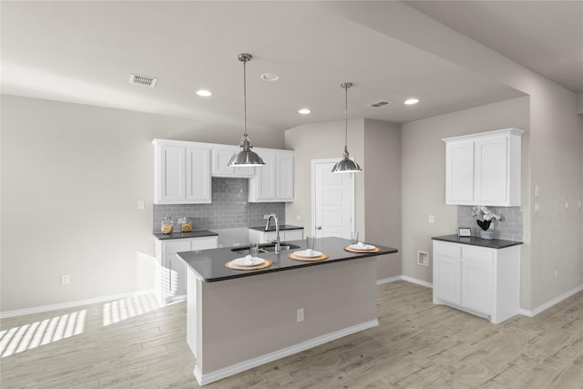 kitchen with decorative backsplash, sink, white cabinetry, and a center island with sink