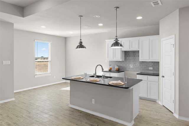 kitchen featuring white cabinets, tasteful backsplash, an island with sink, sink, and hanging light fixtures