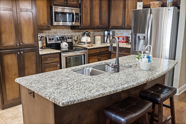 kitchen with a center island with sink, light stone countertops, sink, and appliances with stainless steel finishes