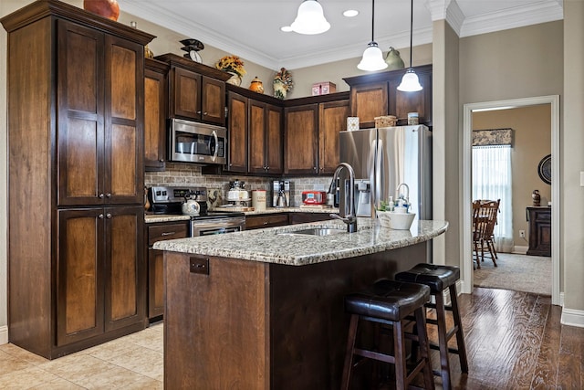 kitchen featuring light stone countertops, stainless steel appliances, sink, a center island with sink, and hanging light fixtures