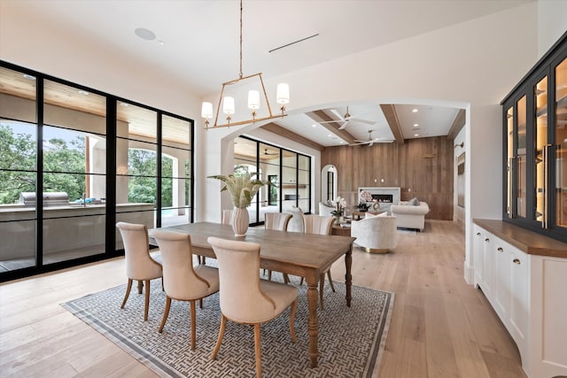 dining room with wooden walls, light wood-type flooring, ceiling fan with notable chandelier, and coffered ceiling