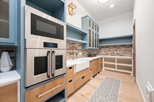 kitchen featuring black microwave, sink, backsplash, light hardwood / wood-style floors, and stainless steel double oven