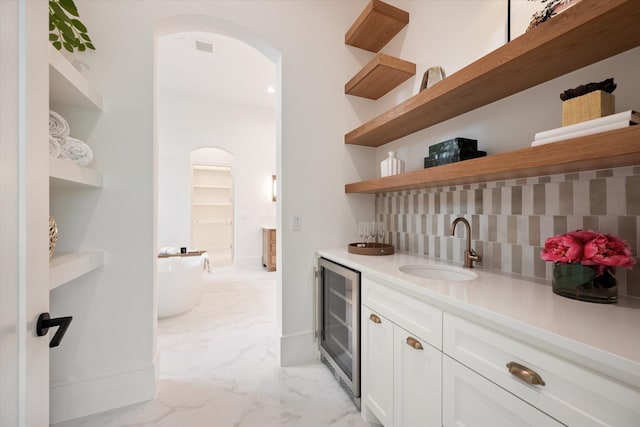 bar with light tile patterned flooring, white cabinets, backsplash, beverage cooler, and sink