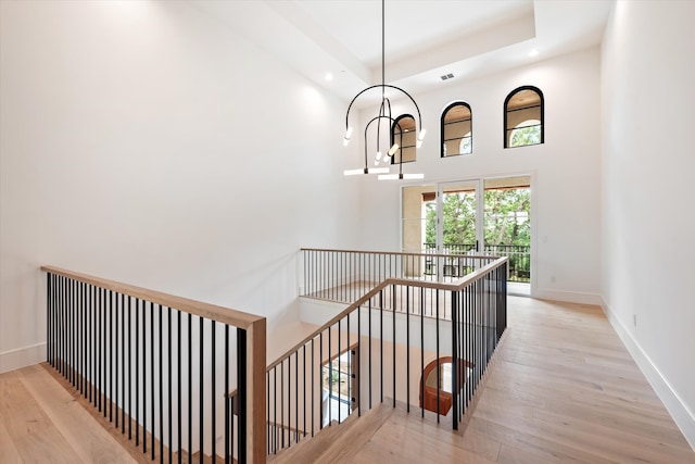 staircase featuring a towering ceiling, a notable chandelier, light wood-type flooring, and a tray ceiling