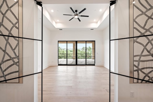 interior space featuring a barn door, light wood-type flooring, ceiling fan, and a raised ceiling