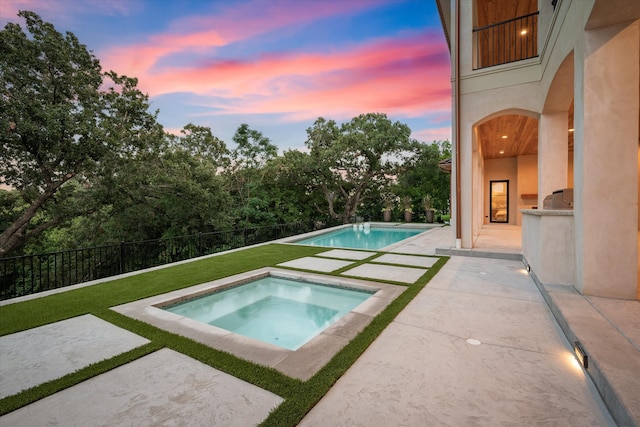 pool at dusk featuring an in ground hot tub and a patio area