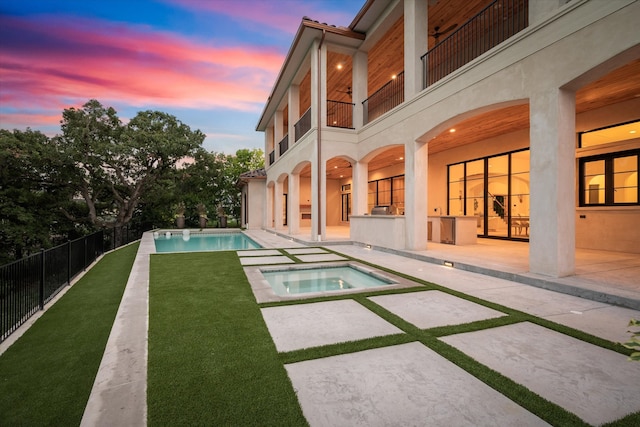 yard at dusk with a balcony, a pool with hot tub, and a patio area