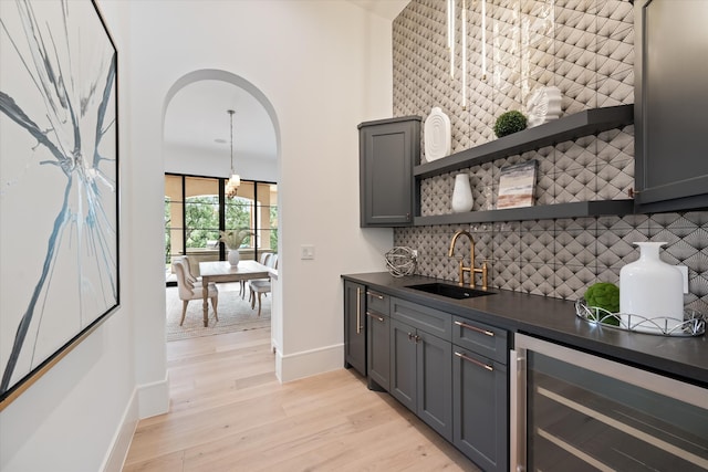 bar featuring tasteful backsplash, gray cabinetry, sink, light hardwood / wood-style floors, and beverage cooler