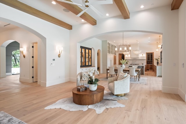 living room featuring beamed ceiling, ceiling fan with notable chandelier, and light hardwood / wood-style floors