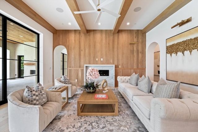 living room featuring beamed ceiling, wood walls, light hardwood / wood-style floors, and ceiling fan