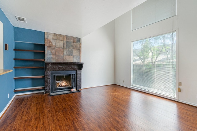 unfurnished living room with built in shelves, a fireplace, and hardwood / wood-style flooring