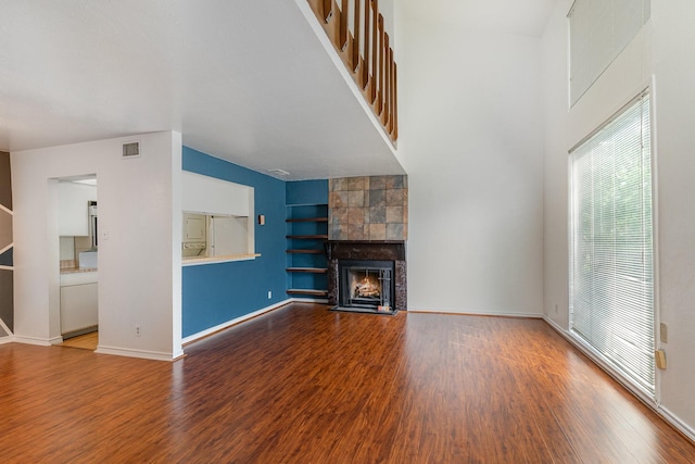 unfurnished living room featuring a tile fireplace, built in features, and hardwood / wood-style floors