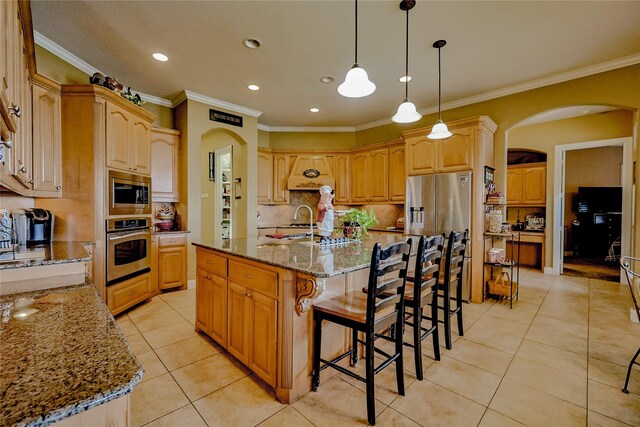 kitchen with appliances with stainless steel finishes, custom exhaust hood, crown molding, light tile patterned floors, and an island with sink