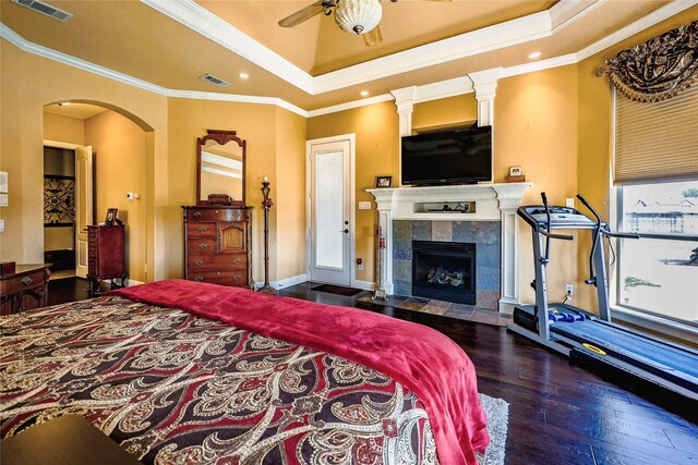 bedroom with a tile fireplace, crown molding, ceiling fan, dark hardwood / wood-style floors, and a tray ceiling