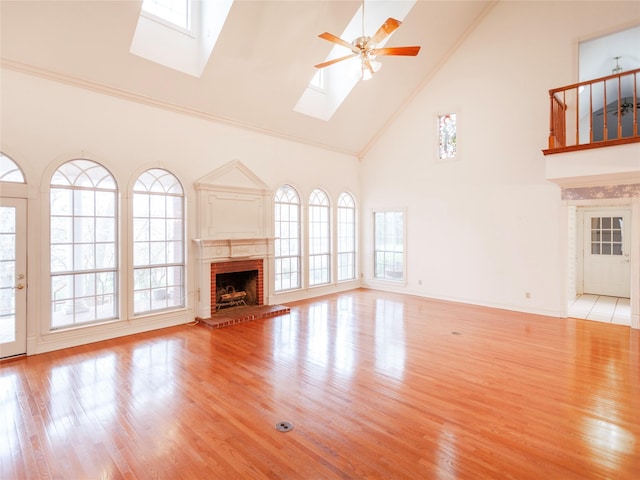 unfurnished living room with high vaulted ceiling, a brick fireplace, a wealth of natural light, and a skylight