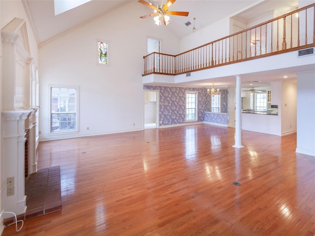 unfurnished living room with ceiling fan with notable chandelier, high vaulted ceiling, a fireplace, and wood-type flooring