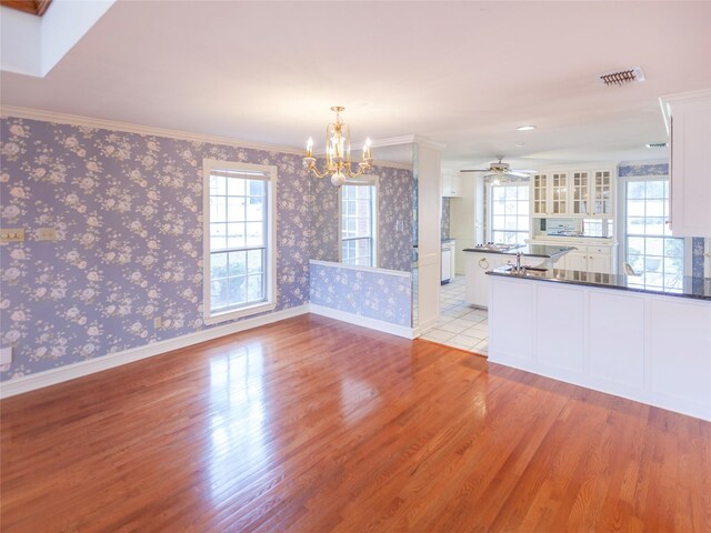 unfurnished living room featuring crown molding, ceiling fan with notable chandelier, light hardwood / wood-style flooring, and a wealth of natural light