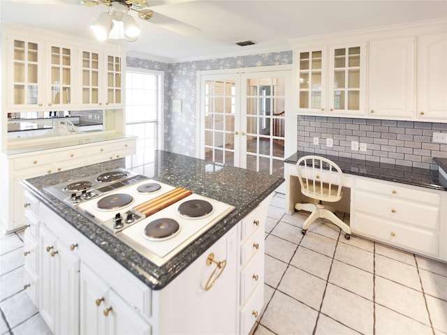 kitchen featuring light tile patterned floors, white cabinets, built in desk, dark stone counters, and white cooktop