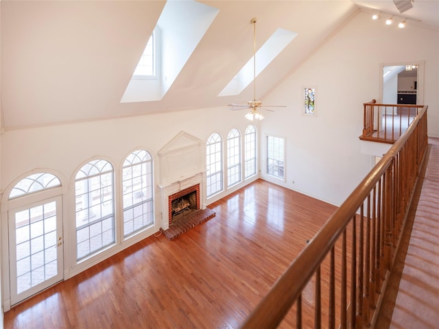 unfurnished living room with a brick fireplace, a healthy amount of sunlight, high vaulted ceiling, and a skylight