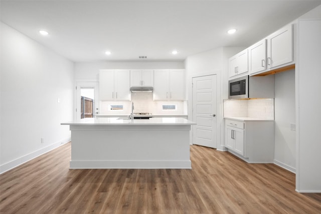 kitchen with backsplash, white cabinetry, built in microwave, and a kitchen island with sink