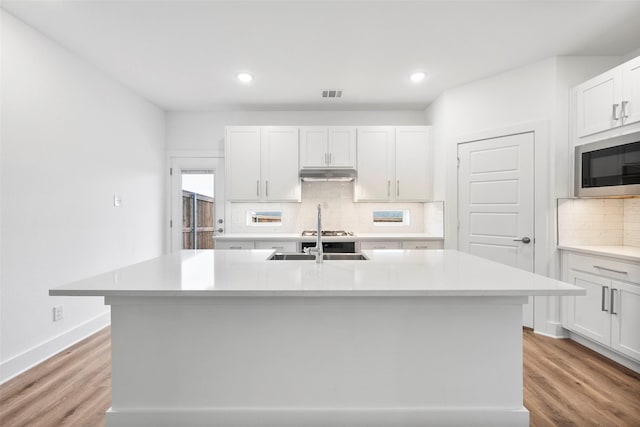 kitchen with an island with sink, sink, white cabinets, and light hardwood / wood-style floors