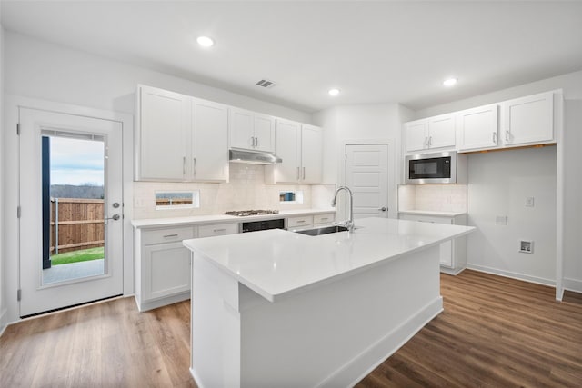 kitchen with built in microwave, white cabinetry, an island with sink, and sink