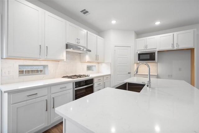 kitchen featuring appliances with stainless steel finishes, backsplash, light stone counters, sink, and white cabinets