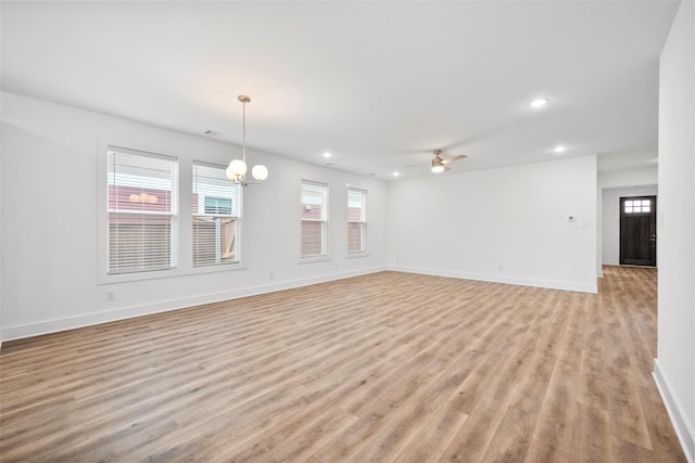 unfurnished living room featuring ceiling fan with notable chandelier and light hardwood / wood-style flooring