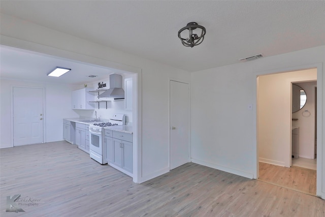 kitchen featuring wall chimney range hood, white gas range oven, light hardwood / wood-style floors, white cabinets, and sink